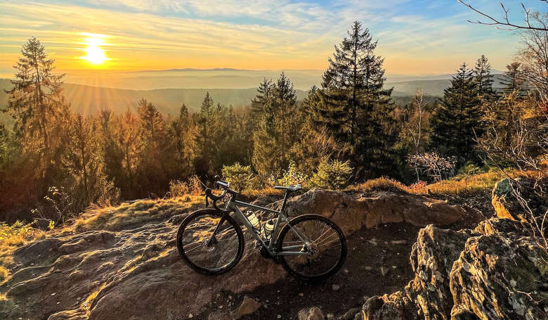 Mountainbike lehnt gegen einen Felsen. Im Hintergrund sieht man die Sonne untergehen.