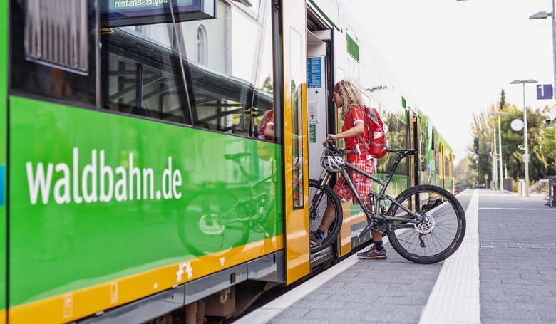 Fahrradfahrerin steigt mit Fahrrad in die Waldbahn ein