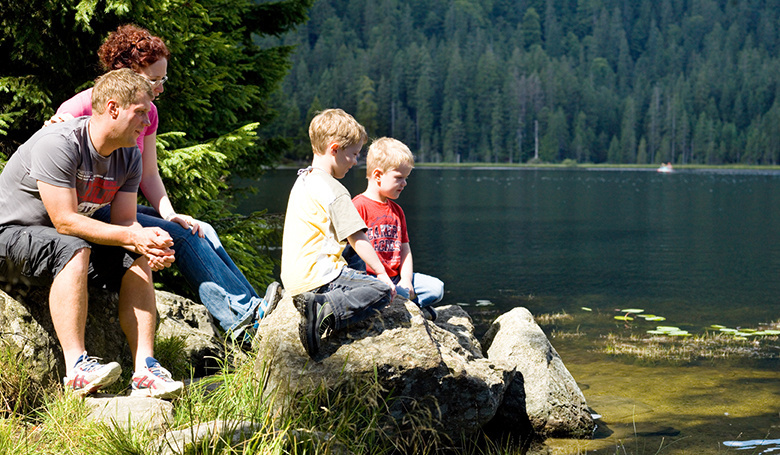 Familie sitzt am See und schaut hinein