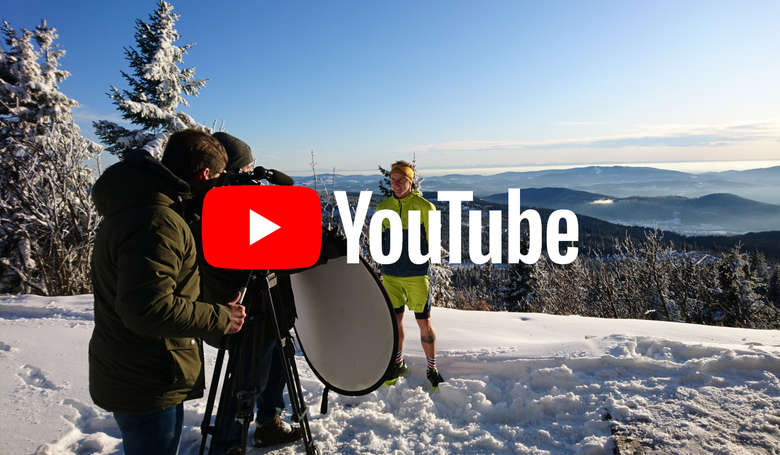 Ein Trailrunner steht im Schnee und wird fotografiert. Das YouTube Logo liegt darüber.