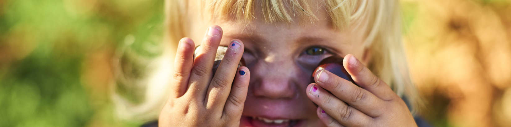 Kind hält sich Kastanien vor die Augen