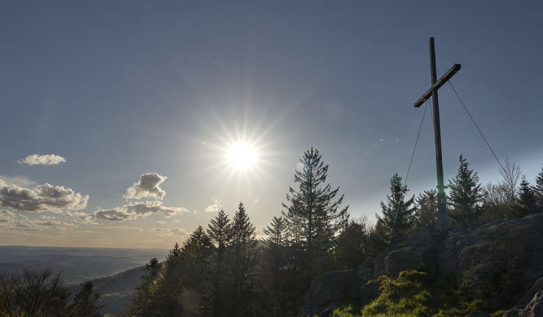 Blick zum Himmel, zur Sonne am Rand steht ein Kreuz